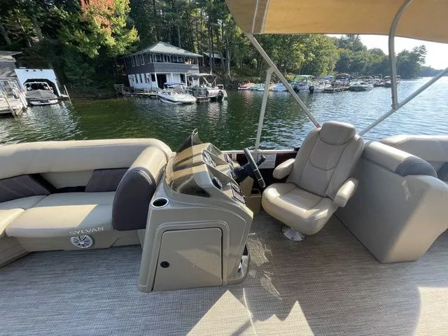 Slide: The Image of 2023 Sylvan 8522 LZ pontoon boat interior with seating and steering console on a lake. - 7