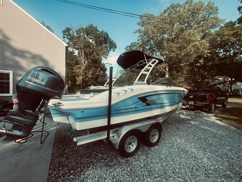 Slide: The Image of 2023 Chaparral 21 SSi OB boat on trailer, parked outdoors near trees and a house. - 25