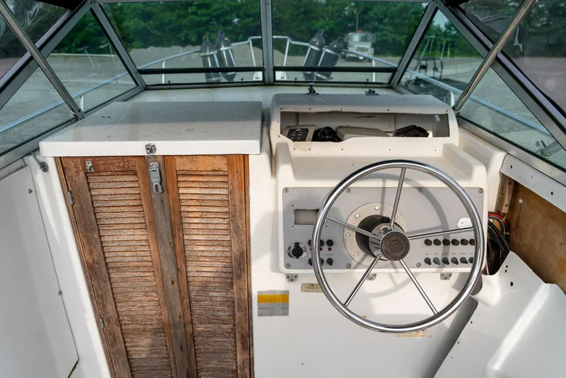 Slide: The Image of 1986 Aquasport 250 Express Fisherman boat cockpit with steering wheel and wooden cabinet. - 18
