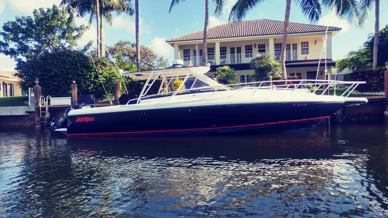 Slide: The Image of 2002 Intrepid 377 Walkaround boat docked by a waterfront house with palm trees. - 0