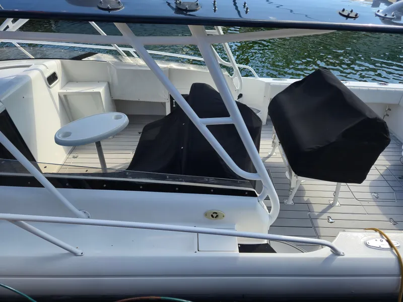 Slide: The Image of 2002 Intrepid 377 Walkaround boat deck with covered seating and table, docked by water. - 12