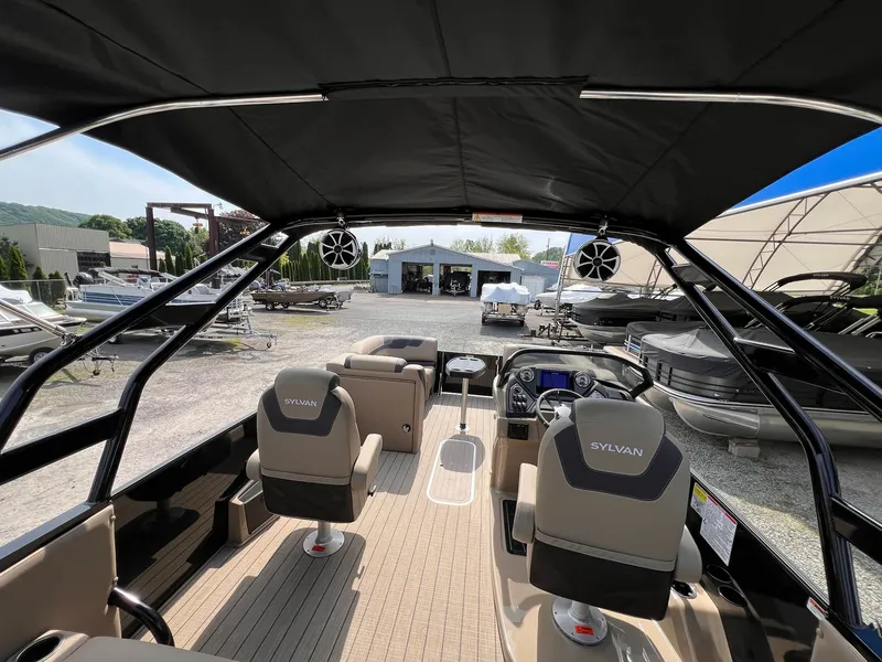 Slide: The Image of 2025 Sylvan L3 CLZ DH WT boat interior with modern seating and dashboard, in a marina setting. - 5