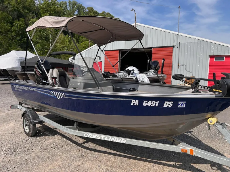 Slide: The Image of 2016 Crestliner 1650 Discovery Side Console boat on trailer, parked near a red and gray building. - 18