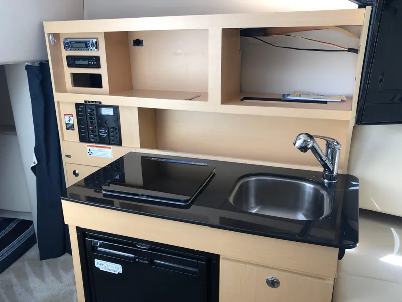 Slide: The Image of 2012 Bayliner 255 Cruiser kitchenette with sink, stove, and storage shelves. - 11