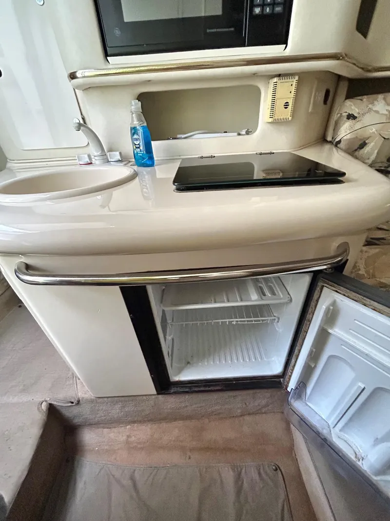 Slide: The Image of 1999 Sea Ray 270 Sundancer kitchenette with sink, stove, and open mini-fridge. - 14