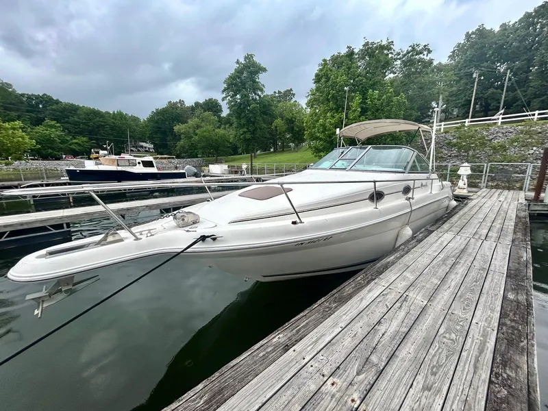 Slide: The Image of 1999 Sea Ray 270 Sundancer docked at a marina, surrounded by lush greenery. - 5