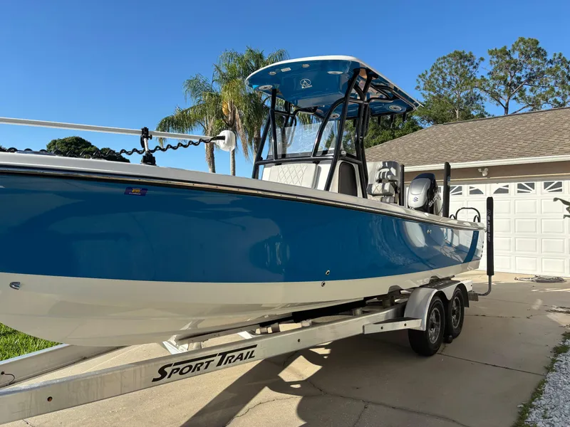 Slide: The Image of 2023 Blazer 2700 HYBRID BAY boat on trailer, blue and white, parked in driveway. - 2