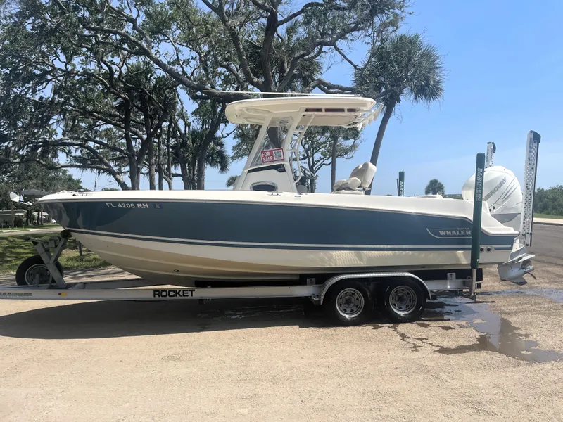Slide: The Image of 2017 Boston Whaler 230 Outrage boat on trailer, parked outdoors under trees. - 4