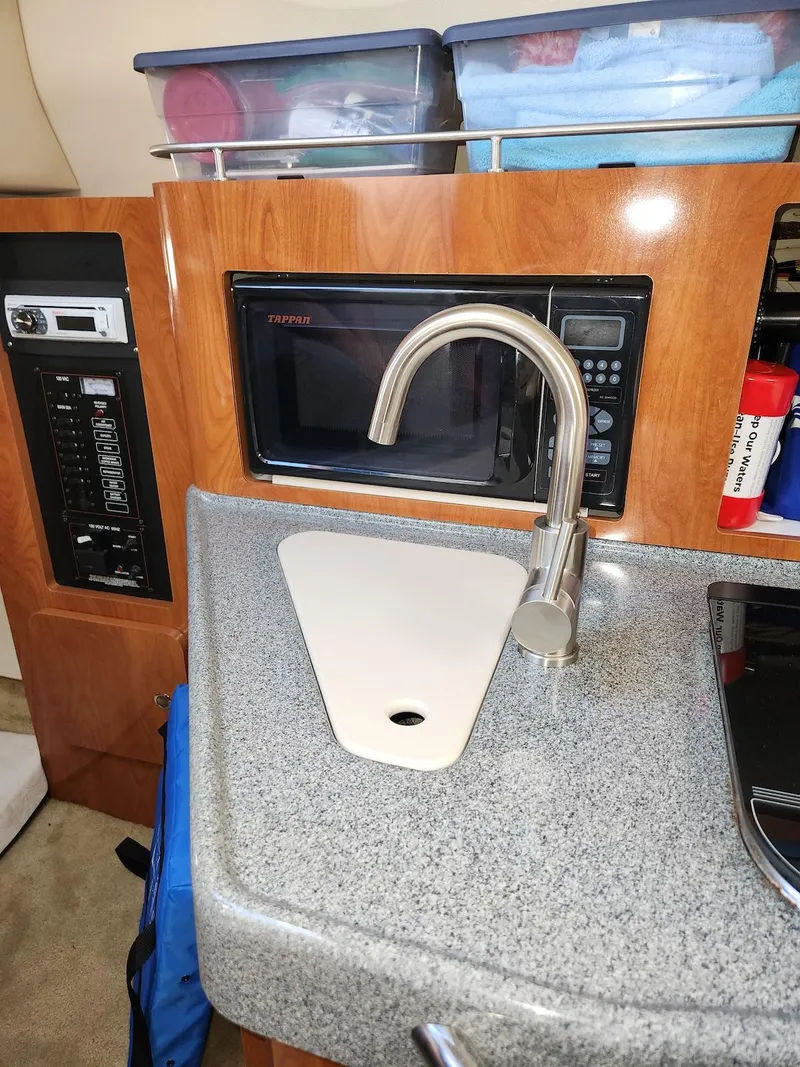 Slide: The Image of 2006 Larson Cabrio 260 boat kitchenette with sink, microwave, and storage containers. - 15