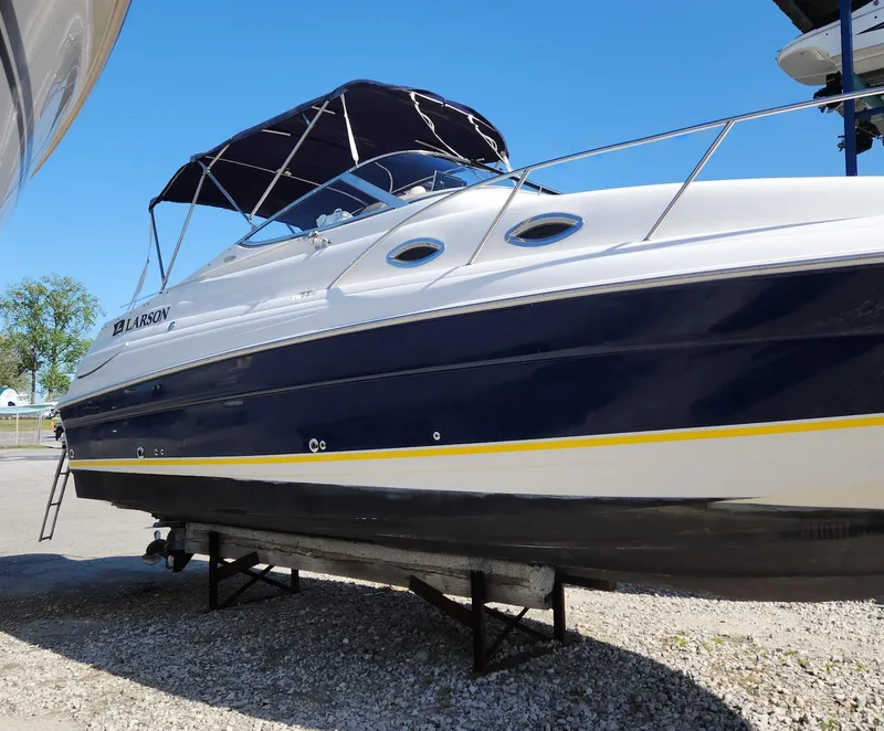 Slide: The Image of 2006 Larson Cabrio 260 boat with blue and white hull, docked on land. - 2