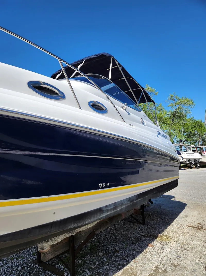 Slide: The Image of 2006 Larson Cabrio 260 boat with blue and white exterior, docked under clear blue sky. - 3