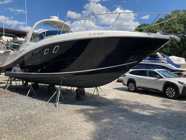 Slide: The Image of 2008 Sea Ray 330 Sundancer yacht on stands, parked beside a car, under a blue sky. - 2