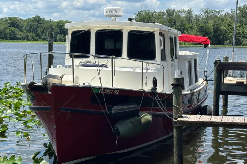 The Image of 1985 Nordic Tug 32 docked on a serene lake with lush greenery. - 0