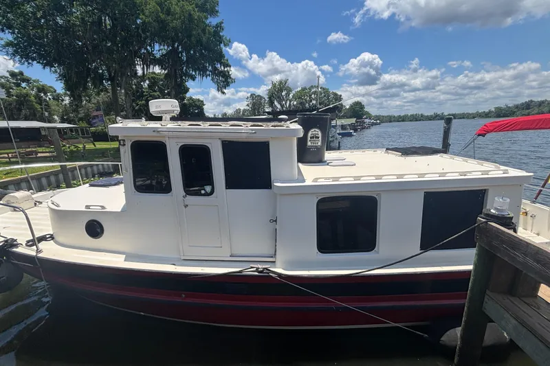 Slide: The Image of 1985 Nordic Tug 32 docked by a scenic lake under a partly cloudy sky. - 2