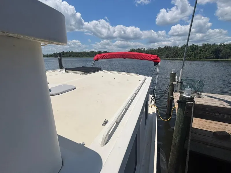 Slide: The Image of 1985 Nordic Tug 32 docked by a scenic lake under a blue sky with clouds. - 4