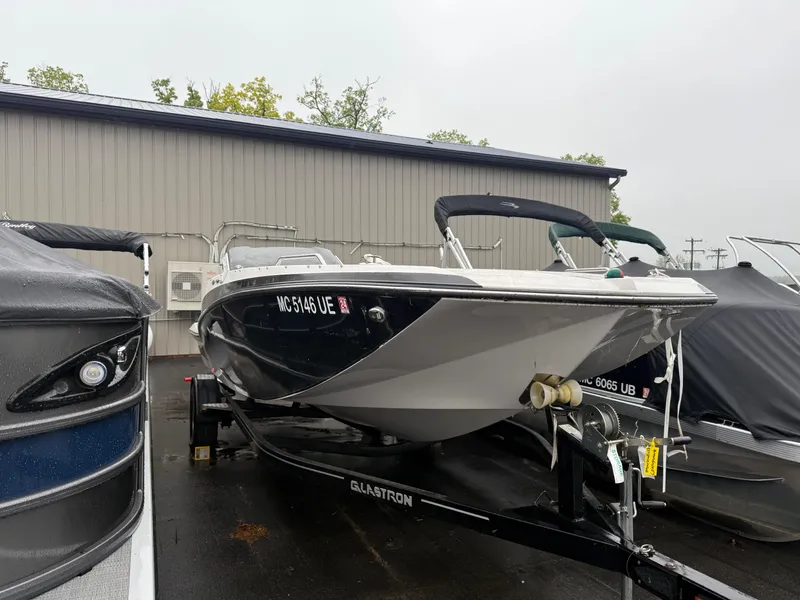 The Image of 2017 Glastron 205 boat on trailer, parked outdoors near a building. - 1
