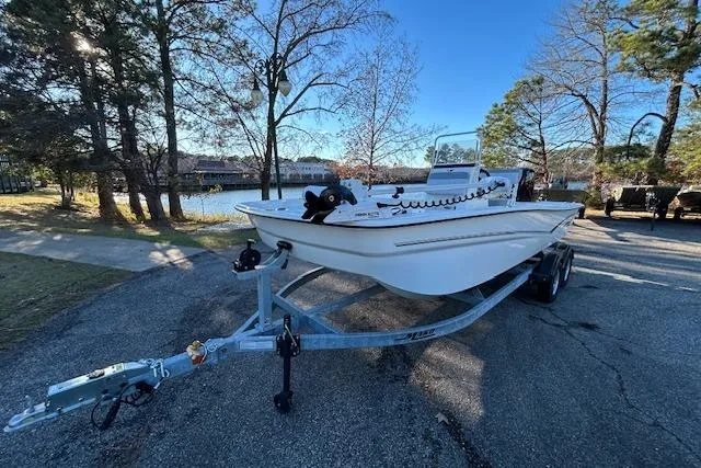 Slide: The Image of 2024 Mako Pro Skiff 19 CC boat on trailer near a lake, surrounded by trees. - 3