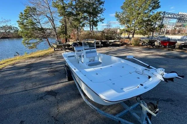 Slide: The Image of 2024 Mako Pro Skiff 19 CC boat on trailer by a lakeside, surrounded by trees. - 7