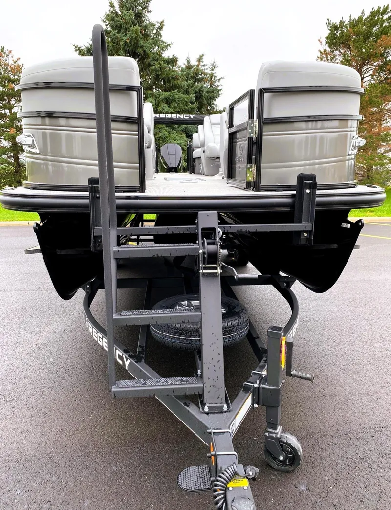 Slide: The Image of 2025 Regency 230 DL3 pontoon boat on trailer, parked on asphalt with trees in background. - 5