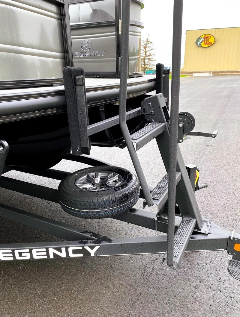 Slide: The Image of 2025 Regency 230 DL3 boat trailer with spare tire, parked near Bass Pro Shops. - 6