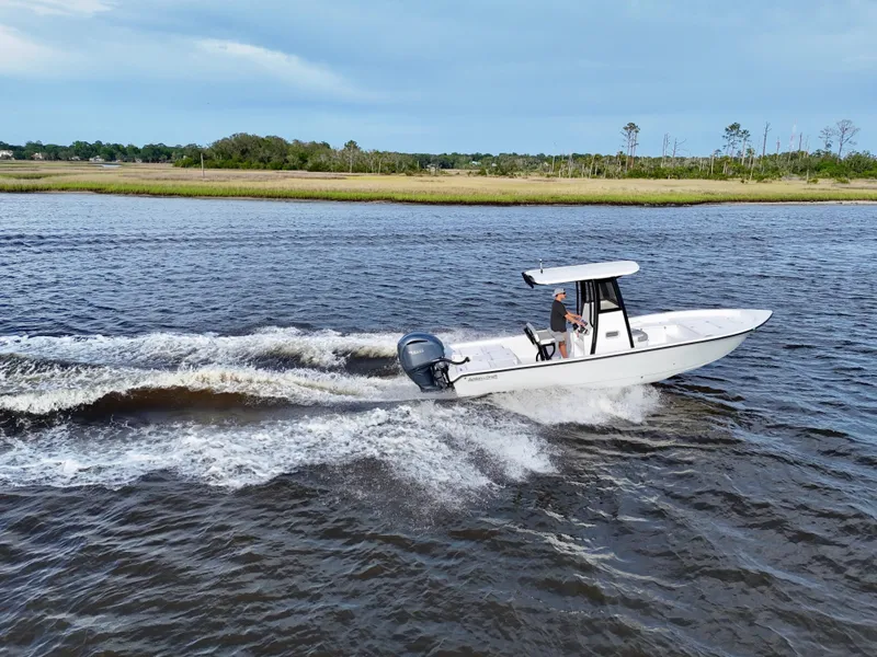 Slide: The Image of 2025 Action Craft 24 Coastal Bay boat cruising on a river with scenic background. - 2