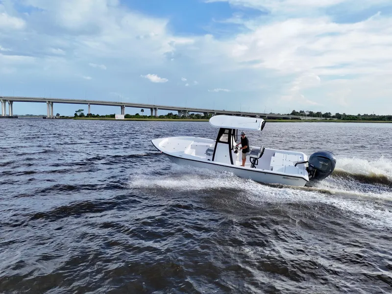 Slide: The Image of 2025 Action Craft 24 Coastal Bay boat cruising on open water near a bridge. - 26