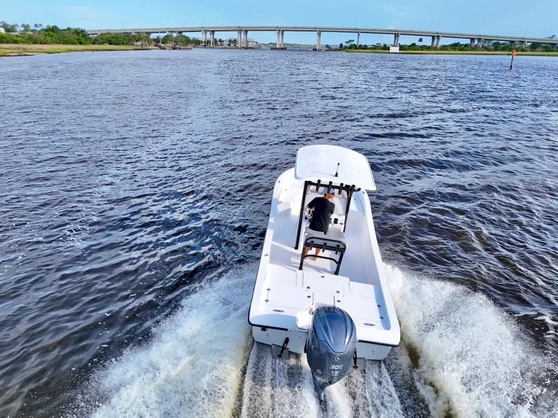 Slide: The Image of 2025 Action Craft 24 Coastal Bay boat cruising on a river with a bridge in the background. - 8