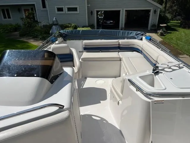 Slide: The Image of 1995 Chaparral 220 Sunseta boat interior with white seating and helm, parked near a house. - 4