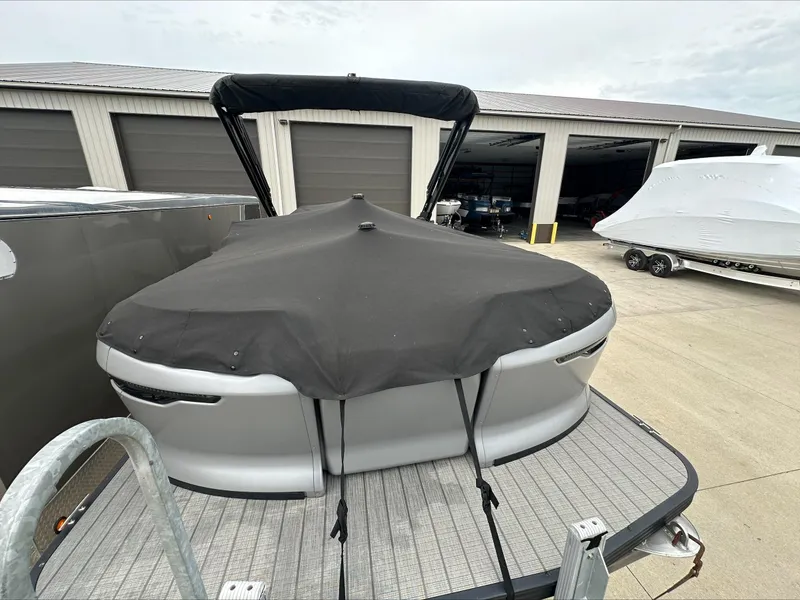 Slide: The Image of 2023 Manitou Explore boat with cover in storage facility. - 2