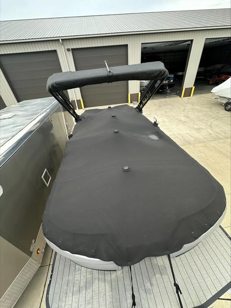Slide: The Image of 2023 Manitou Explore boat with black cover in storage facility. - 3