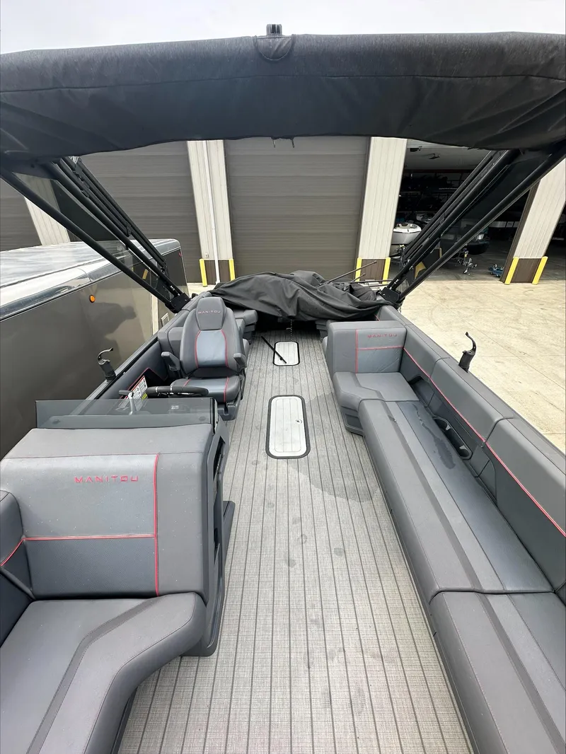 Slide: The Image of 2023 Manitou Explore boat interior with gray seating and canopy, docked near storage units. - 8