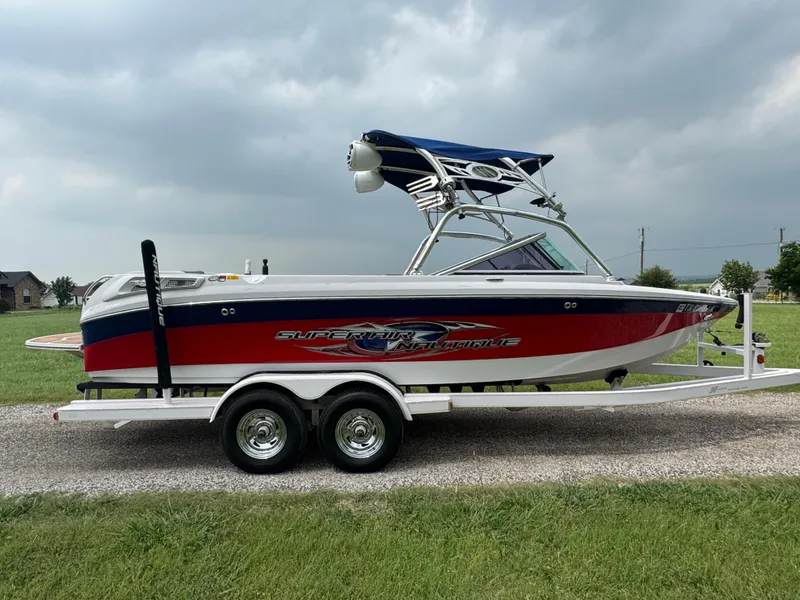 Slide: The Image of 2007 Nautique Super Air Nautique 230 boat on trailer, red and white design, parked on grass. - 4