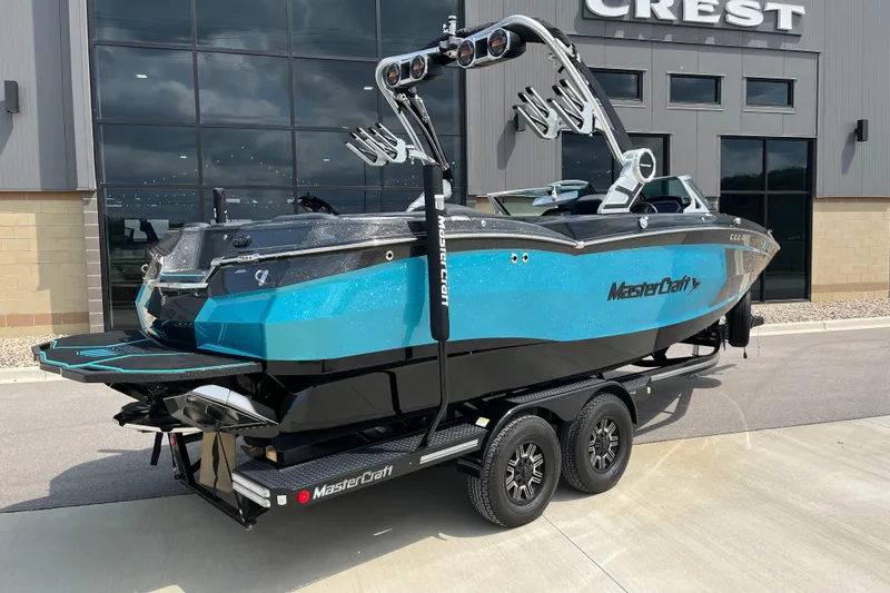 Slide: The Image of 2018 MasterCraft XStar boat on trailer, blue and black design, parked outside a building. - 3