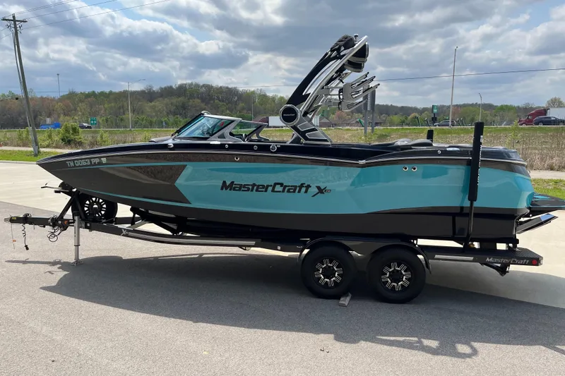 Slide: The Image of 2018 MasterCraft XStar boat on trailer, turquoise and black design, parked outdoors. - 5