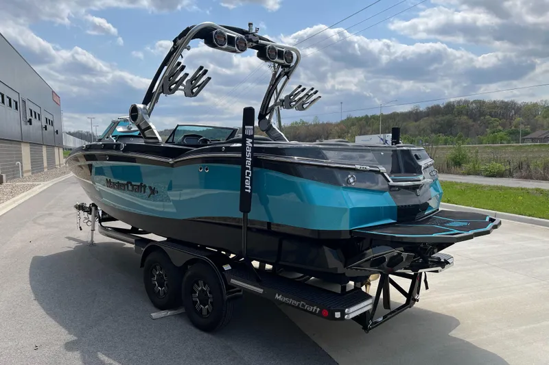 Slide: The Image of 2018 MasterCraft XStar boat on trailer, blue and black design, parked outdoors. - 6
