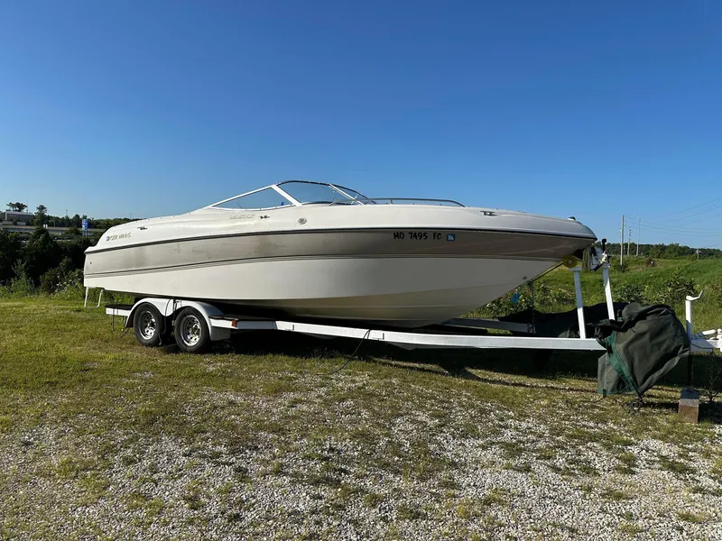 The Image of 1997 Four Winns 240 Horizon boat on trailer, parked on grassy area under clear blue sky. - 1