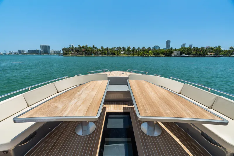 Slide: The Image of Luxurious 2019 CNM Continental 54T yacht deck with wooden tables, overlooking serene waters and cityscape. - 20