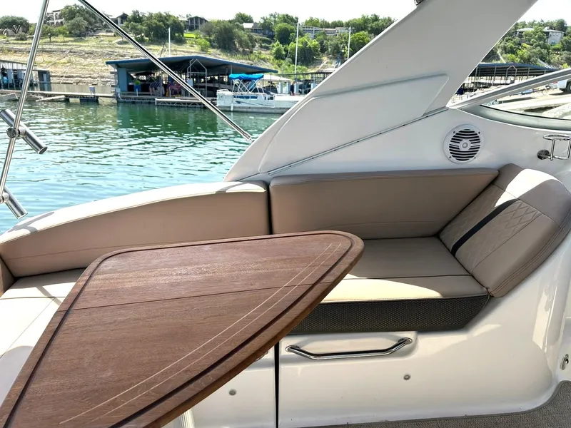 Slide: The Image of 2017 Sea Ray 280 Sundancer interior with cushioned seating and wooden table by the water. - 25
