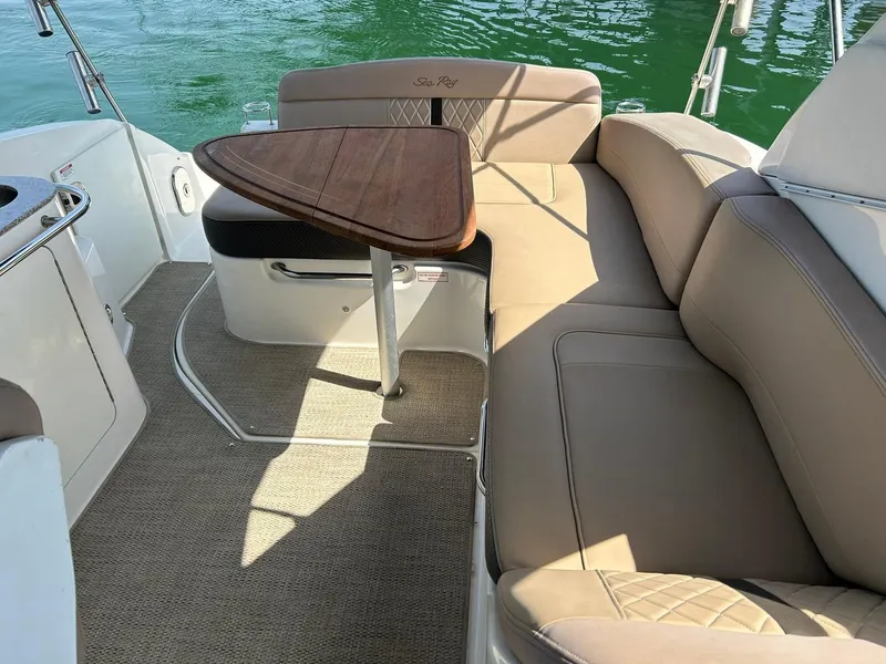 Slide: The Image of 2017 Sea Ray 280 Sundancer interior with beige seating and wooden table on a sunny day. - 29