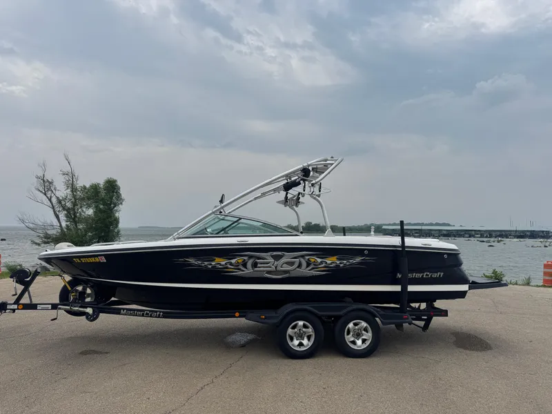 Slide: The Image of 2006 MasterCraft X30 boat on trailer by a lake under cloudy sky. - 1