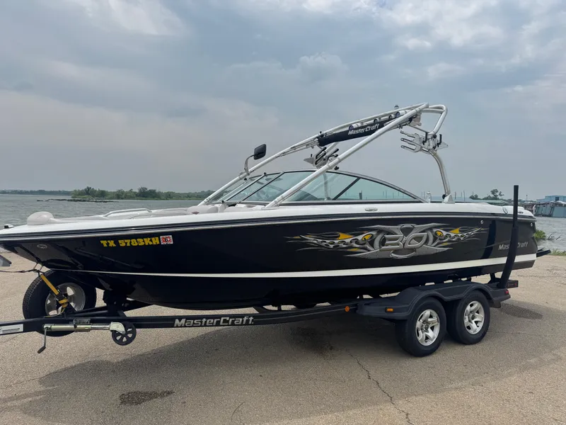 Slide: The Image of 2006 MasterCraft X30 boat on trailer by a lake under cloudy sky. - 2
