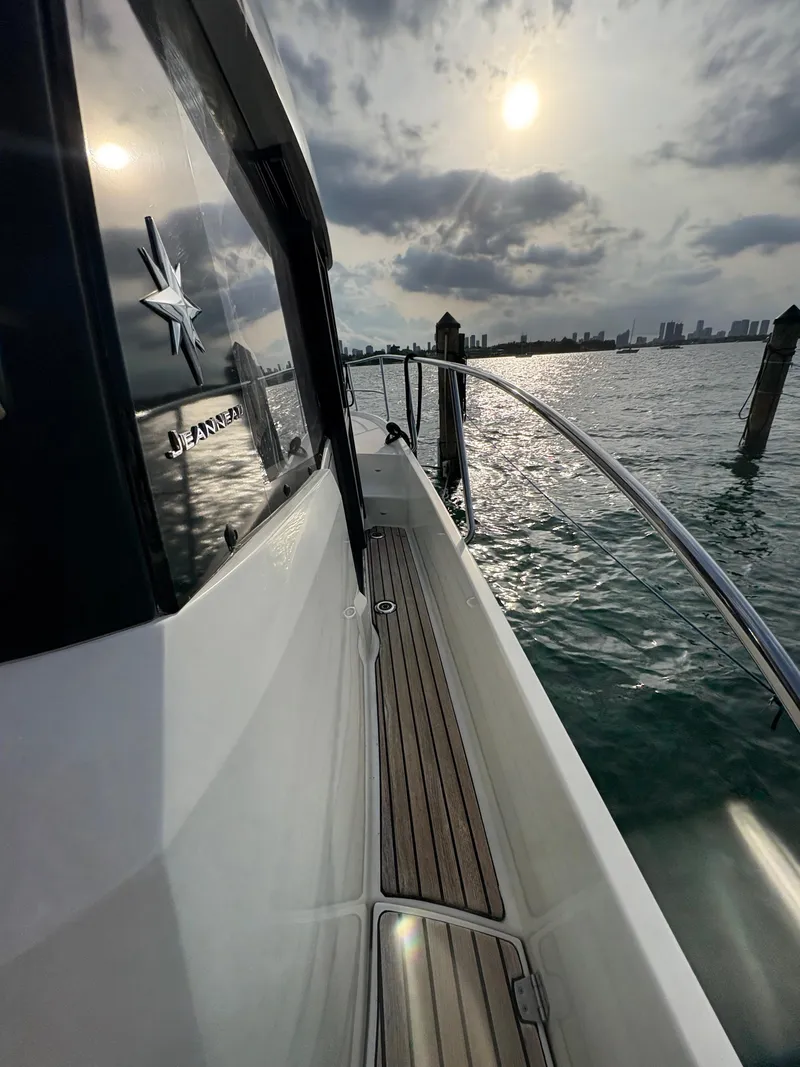Slide: The Image of 2018 Jeanneau Merry Fisher 855 boat on water at sunset, with city skyline. - 30