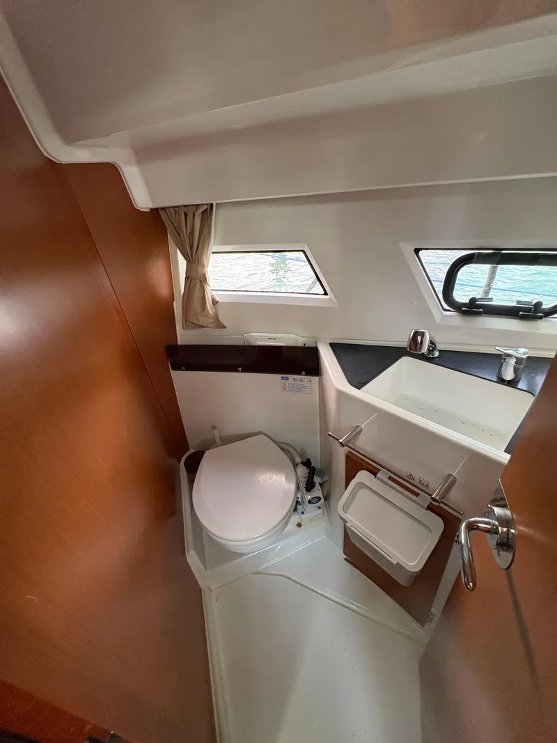 Slide: The Image of 2018 Jeanneau Merry Fisher 855 boat bathroom with toilet, sink, and porthole windows. - 33