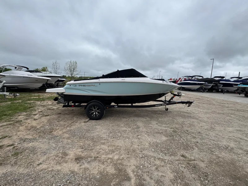Slide: The Image of 2021 Regal 1900 ES boat on trailer, parked outdoors under cloudy sky. - 0