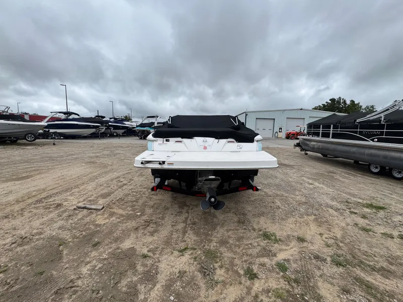 Slide: The Image of 2021 Regal 1900 ES boat, covered, parked on gravel lot with other boats. - 1