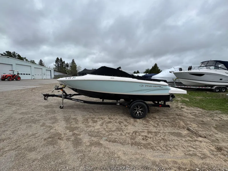 Slide: The Image of 2021 Regal 1900 ES boat on trailer, parked outdoors under cloudy sky. - 2