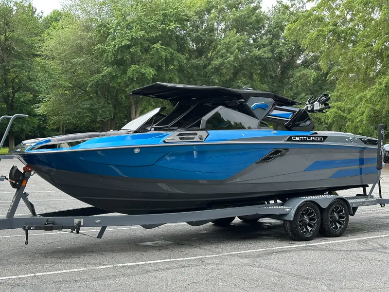 Slide: The Image of 2025 Centurion Ri245 boat in blue and gray on a trailer, parked outdoors. - 18