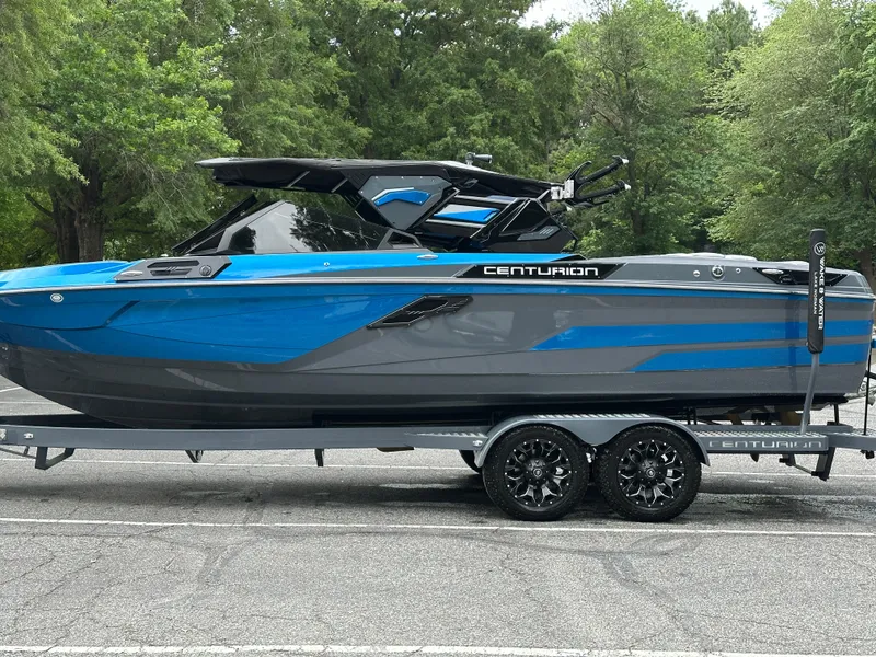 Slide: The Image of 2025 Centurion Ri245 boat in blue and gray on a trailer, parked outdoors. - 19