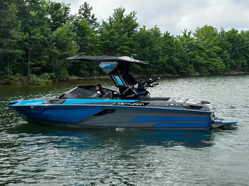 Slide: The Image of 2025 Centurion Ri245 boat on a lake with lush green trees in the background. - 2
