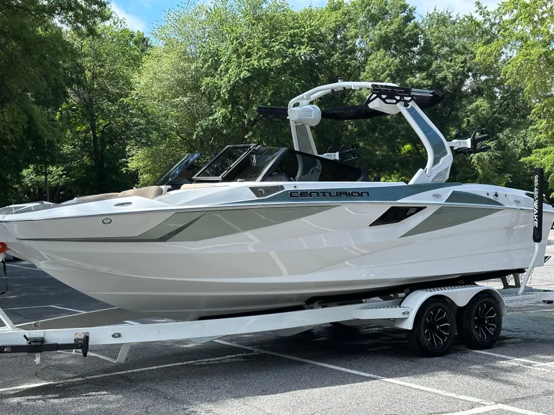Slide: The Image of 2025 Centurion Fe23 boat on trailer, parked outdoors, surrounded by trees. - 13